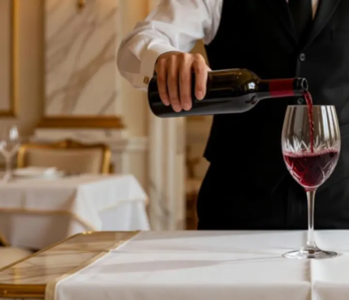 Sommelier a servir vinho tinto em copo de cristal sobre mesa elegantemente posta.